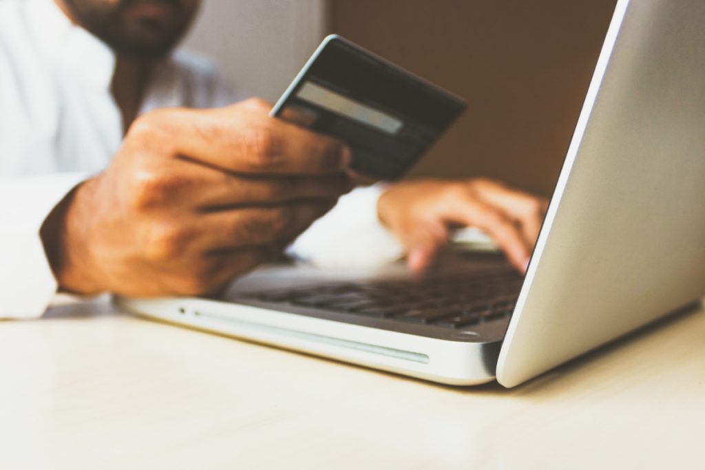 Man holding a credit card next to a laptop showing ecommerce in action